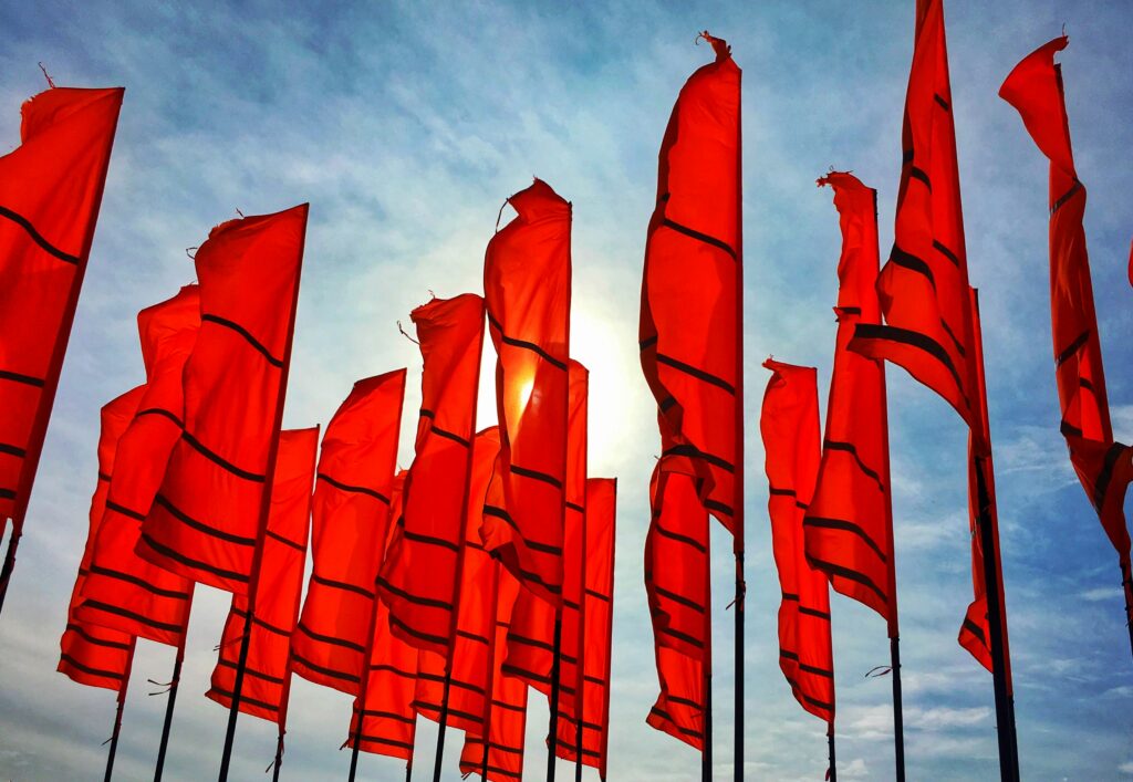 Multiple red flags waving against blue sky representing hidden system costs warning signs